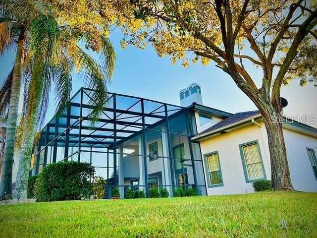 back of house featuring a lanai, a lawn, and stucco siding