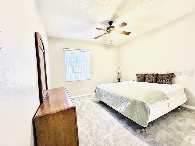 bedroom featuring ceiling fan, a textured ceiling, baseboards, and carpet flooring