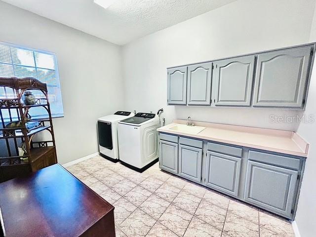 laundry area featuring a textured ceiling, a sink, baseboards, cabinet space, and washer and clothes dryer