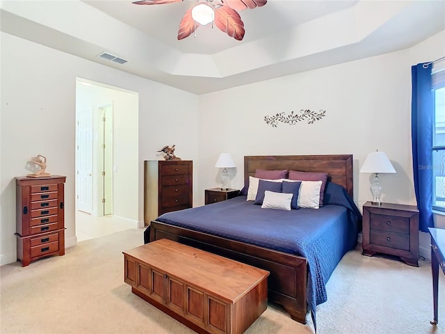 bedroom featuring a raised ceiling, light carpet, and ceiling fan