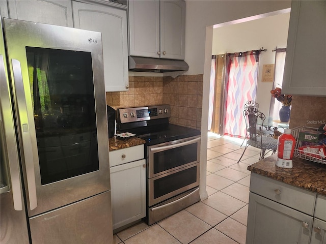 kitchen with dark stone countertops, white cabinets, backsplash, light tile patterned floors, and stainless steel appliances