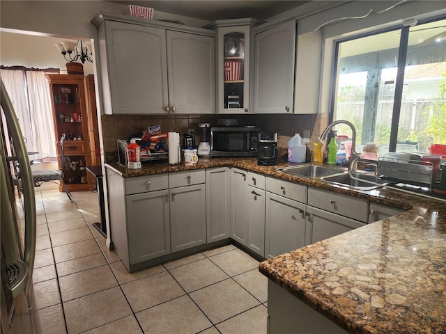 kitchen with gray cabinets, light tile patterned flooring, tasteful backsplash, sink, and dark stone countertops