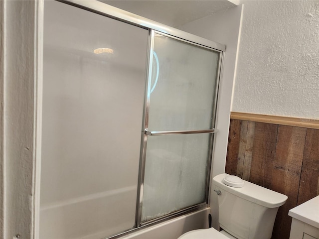 full bathroom with shower / bath combination with glass door, vanity, wooden walls, and toilet