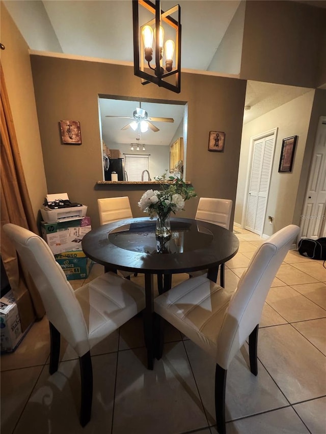 dining space with ceiling fan with notable chandelier, vaulted ceiling, and light tile patterned floors