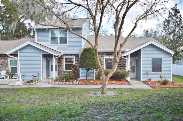 view of front of property featuring brick siding, a front lawn, and roof with shingles