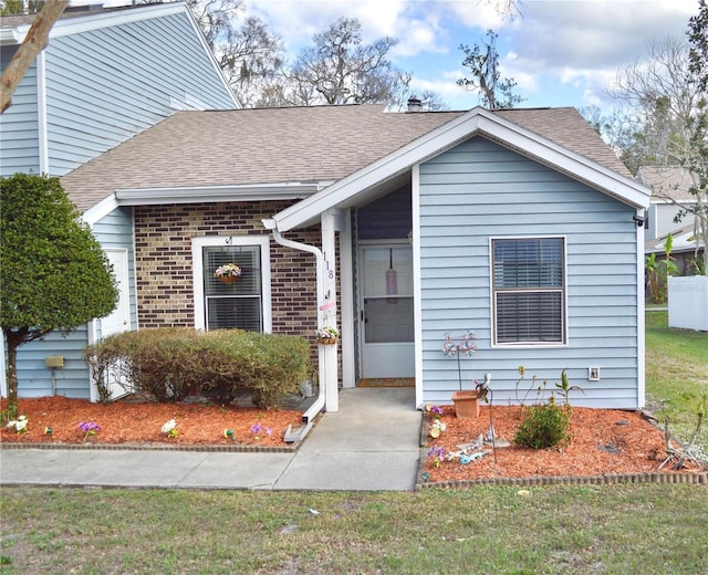 view of front of home featuring brick siding, a shingled roof, and a front yard