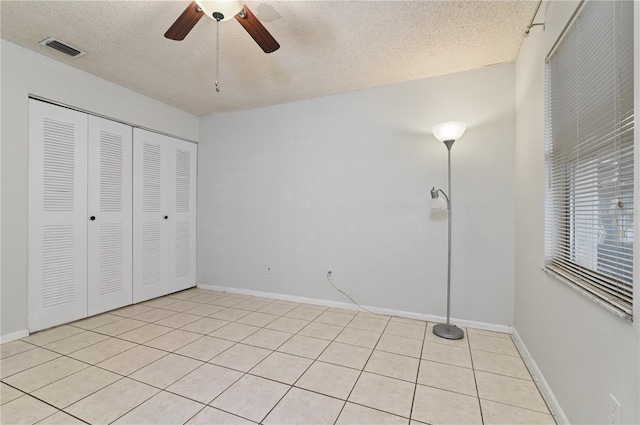 unfurnished bedroom featuring ceiling fan, a closet, a textured ceiling, and light tile patterned floors