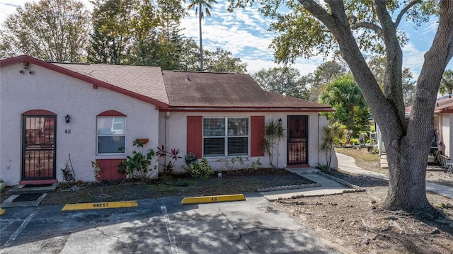 view of front of house with uncovered parking, stucco siding, and a shingled roof