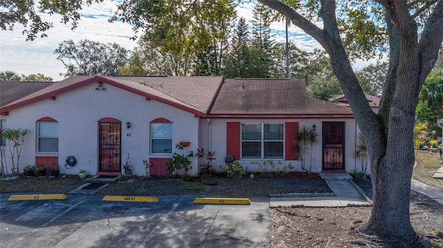 view of front of property featuring stucco siding, roof with shingles, and uncovered parking