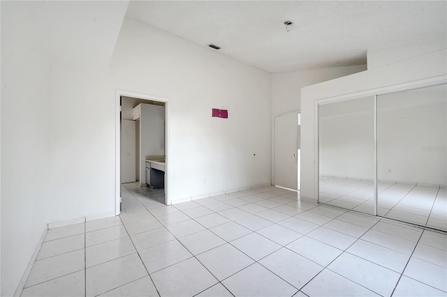 unfurnished bedroom featuring light tile patterned flooring, connected bathroom, high vaulted ceiling, and a closet