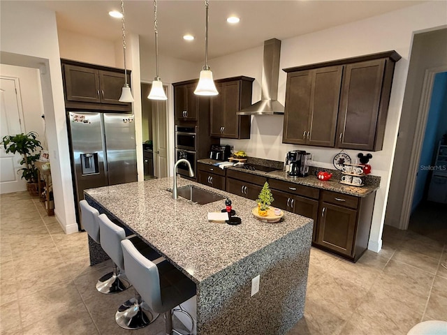 kitchen with sink, a kitchen island with sink, hanging light fixtures, stainless steel appliances, and wall chimney exhaust hood