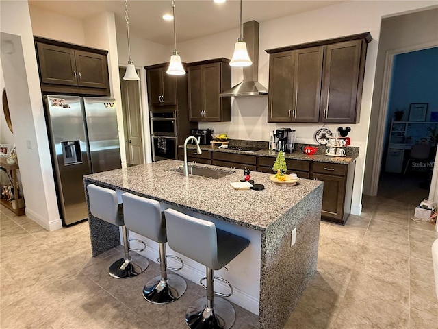 kitchen featuring sink, hanging light fixtures, stainless steel appliances, light stone counters, and wall chimney exhaust hood