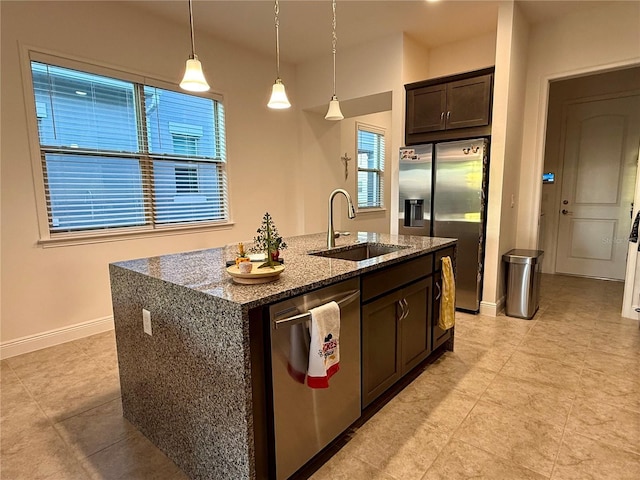 kitchen featuring sink, appliances with stainless steel finishes, dark stone countertops, a kitchen island with sink, and dark brown cabinets