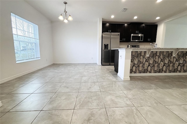 kitchen featuring a kitchen bar, light stone counters, kitchen peninsula, pendant lighting, and stainless steel appliances