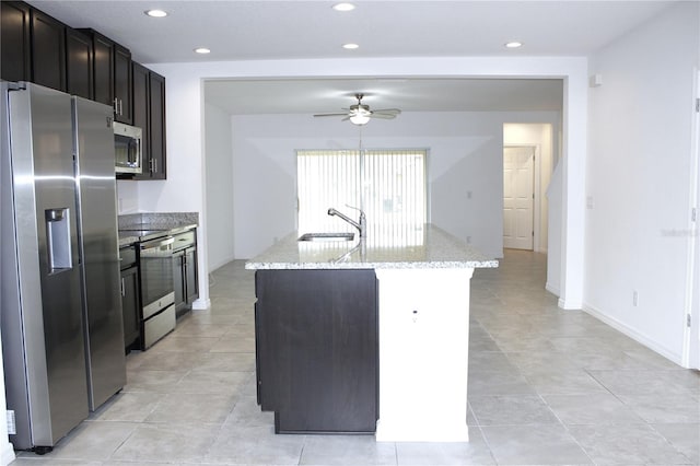 kitchen featuring an island with sink, sink, ceiling fan, light stone counters, and stainless steel appliances