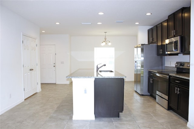 kitchen with sink, a kitchen island with sink, hanging light fixtures, stainless steel appliances, and light stone countertops