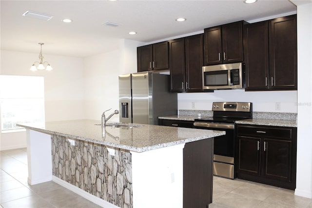 kitchen featuring sink, hanging light fixtures, light stone counters, stainless steel appliances, and a center island with sink