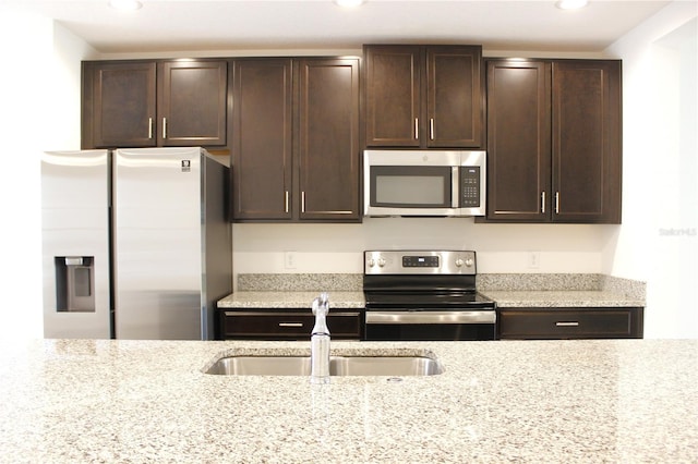 kitchen with dark brown cabinetry, appliances with stainless steel finishes, light stone countertops, and sink