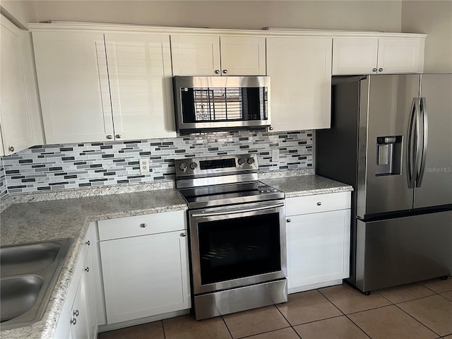 kitchen with sink, light tile patterned floors, appliances with stainless steel finishes, white cabinetry, and backsplash