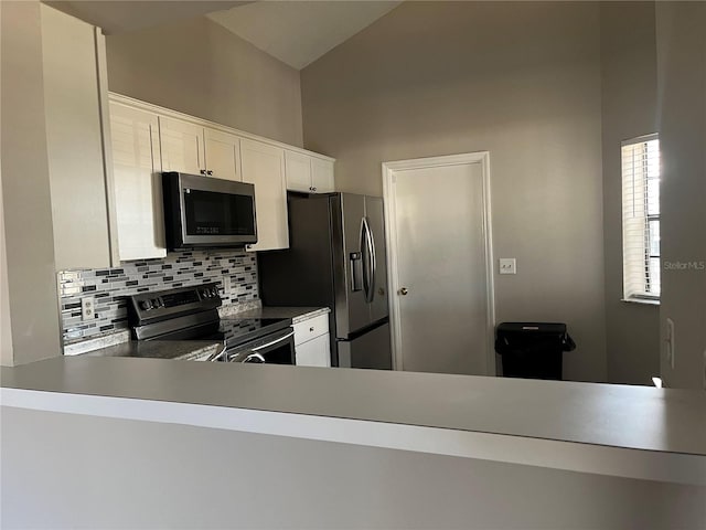 kitchen featuring tasteful backsplash, vaulted ceiling, kitchen peninsula, stainless steel appliances, and white cabinets