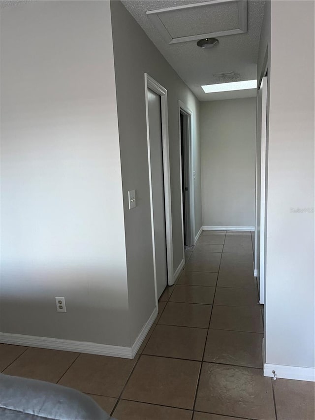 hall with a textured ceiling and dark tile patterned floors