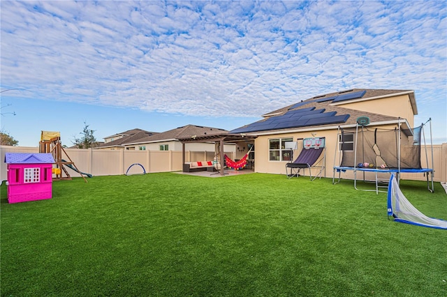 back of house with a playground, a patio, a trampoline, a yard, and solar panels