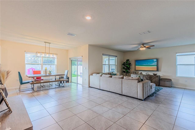 living room featuring light tile patterned floors, ceiling fan with notable chandelier, and a textured ceiling