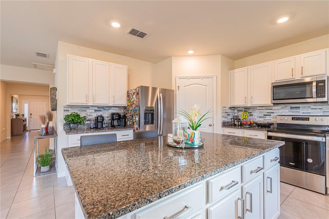 kitchen featuring white cabinetry, appliances with stainless steel finishes, a kitchen island, and dark stone counters