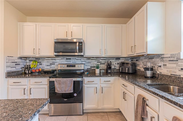 kitchen with light tile patterned flooring, appliances with stainless steel finishes, dark stone countertops, white cabinets, and decorative backsplash