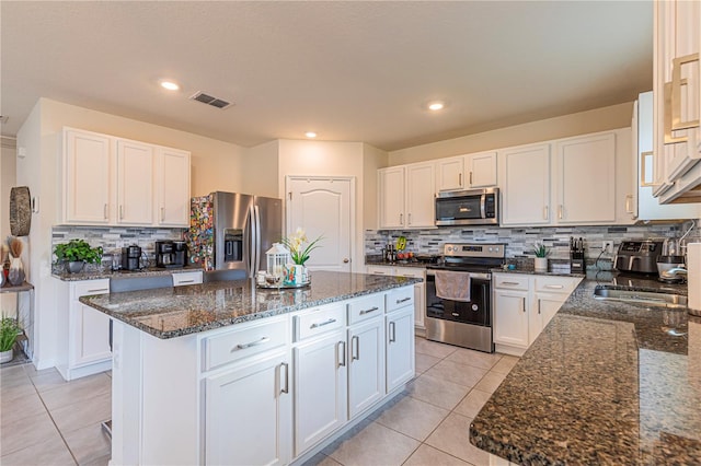 kitchen with dark stone countertops, light tile patterned floors, appliances with stainless steel finishes, a kitchen island, and white cabinets