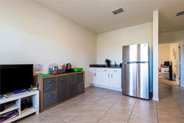 kitchen with dark brown cabinetry, white cabinetry, light tile patterned floors, stainless steel refrigerator, and dark stone counters