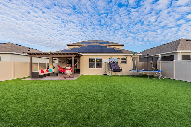 rear view of house with solar panels, a trampoline, a yard, an outdoor living space, and a patio