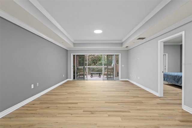 empty room featuring baseboards, a raised ceiling, light wood-style floors, and ornamental molding