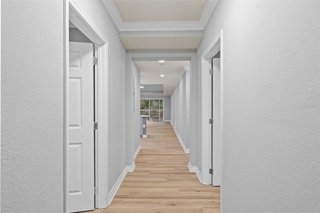 corridor with a textured wall, crown molding, light wood finished floors, and baseboards