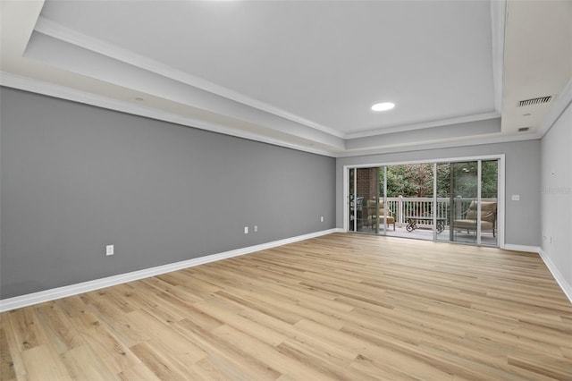 unfurnished living room with crown molding, visible vents, a raised ceiling, baseboards, and light wood finished floors