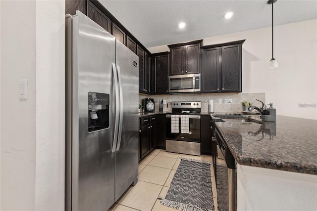 kitchen featuring appliances with stainless steel finishes, tasteful backsplash, light tile patterned floors, dark stone countertops, and pendant lighting