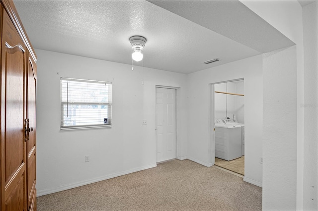 unfurnished bedroom featuring light colored carpet, separate washer and dryer, and a textured ceiling