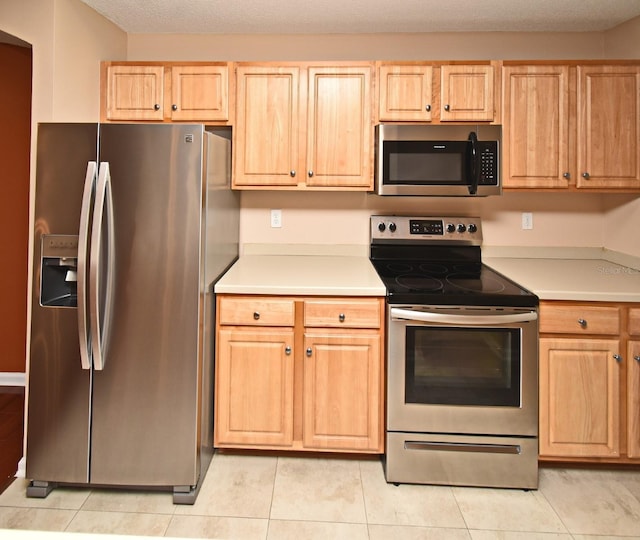 kitchen with light tile patterned floors, stainless steel appliances, a textured ceiling, and light brown cabinets