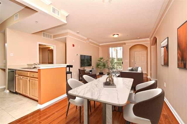 dining room featuring crown molding, sink, a textured ceiling, and light wood-type flooring