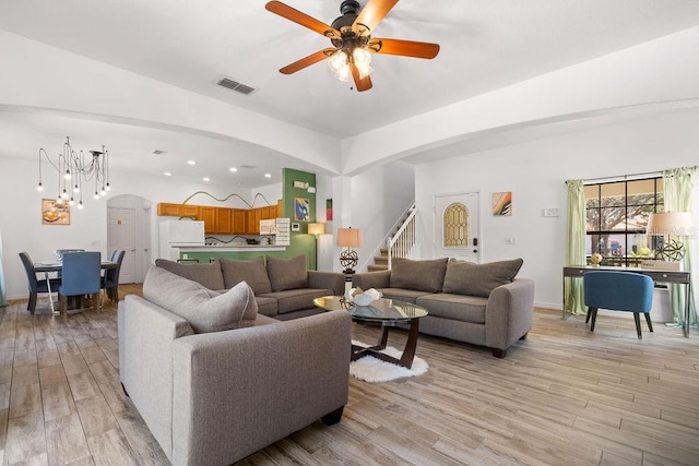 living room featuring ceiling fan with notable chandelier and light hardwood / wood-style flooring