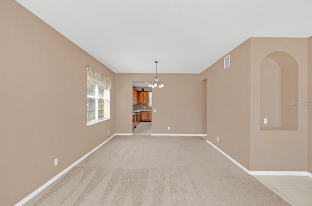 spare room with light colored carpet and an inviting chandelier