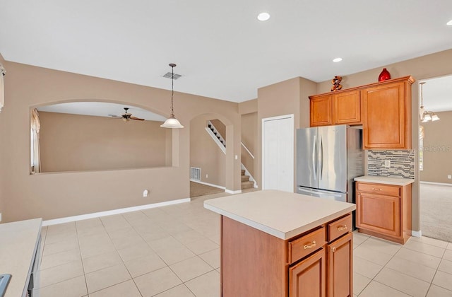 kitchen featuring light tile patterned flooring, stainless steel refrigerator, decorative light fixtures, tasteful backsplash, and a center island