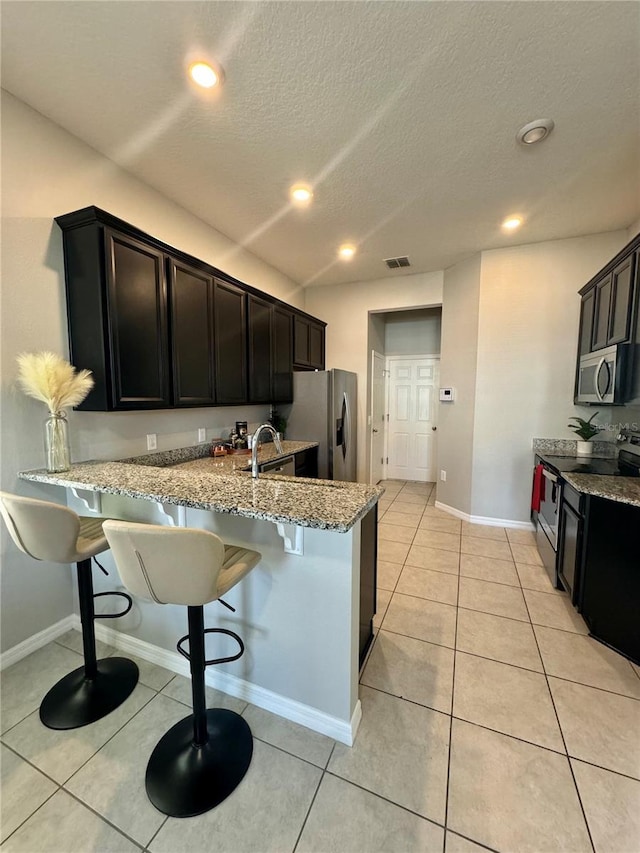 kitchen featuring a breakfast bar, stainless steel appliances, light stone counters, light tile patterned flooring, and kitchen peninsula