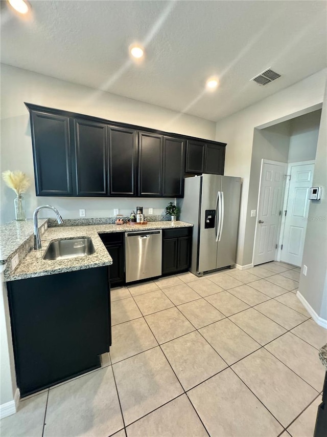 kitchen with sink, light tile patterned floors, light stone countertops, and appliances with stainless steel finishes