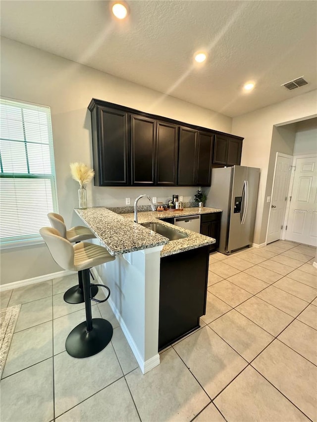 kitchen with a breakfast bar, sink, appliances with stainless steel finishes, kitchen peninsula, and light stone countertops