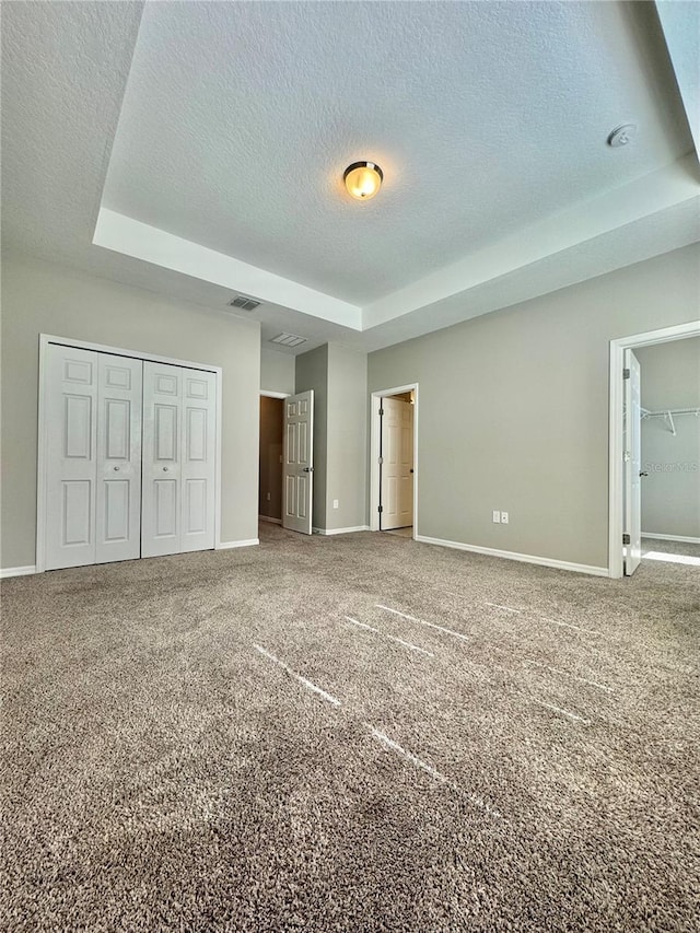 unfurnished bedroom with a raised ceiling, carpet floors, a closet, and a textured ceiling