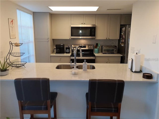 kitchen featuring appliances with stainless steel finishes, sink, gray cabinetry, a kitchen bar, and decorative backsplash