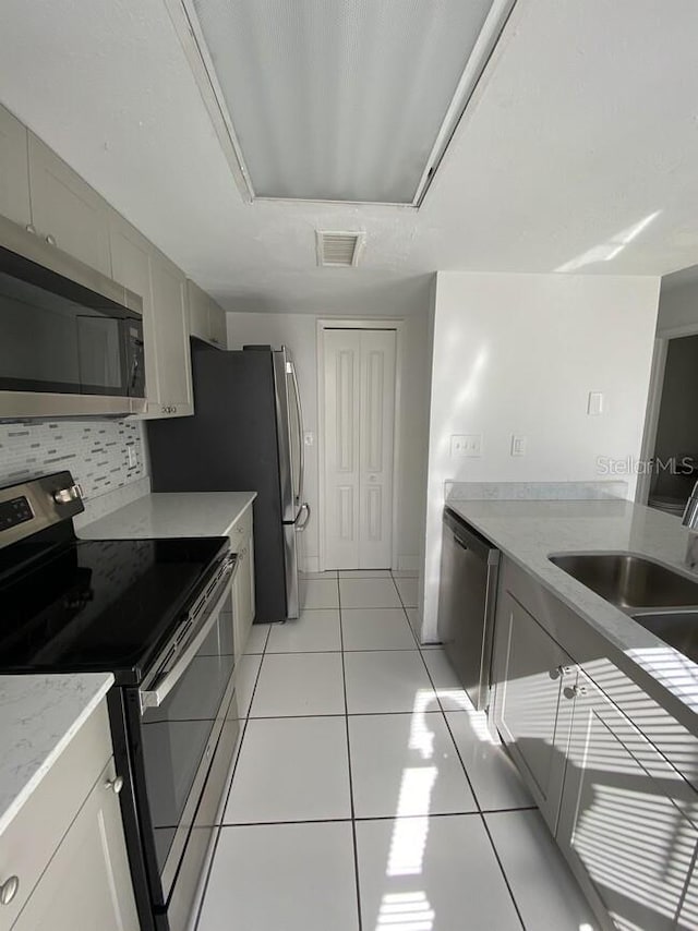 kitchen featuring tasteful backsplash, light tile patterned floors, stainless steel appliances, and sink