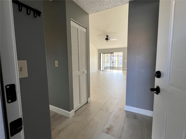 corridor with a textured ceiling and light wood-type flooring