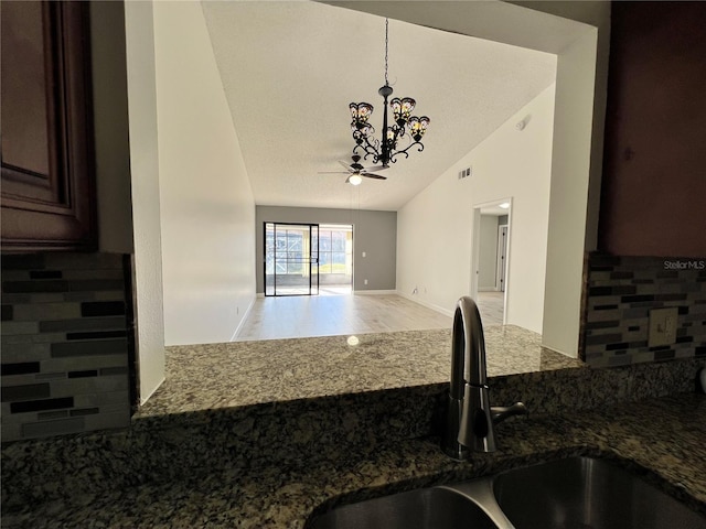 kitchen featuring lofted ceiling, sink, dark stone countertops, backsplash, and decorative light fixtures